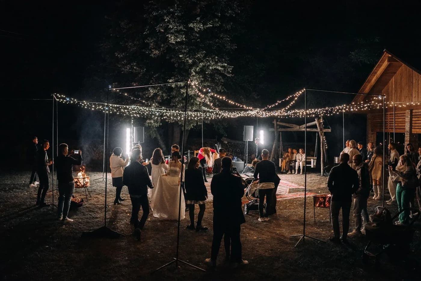 Guests at an outdoor evening reception lit by string lights