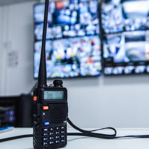 A two-way radio on a desk in front of CCTV monitors